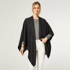 A person wears a black COCO + CARMEN Kiara Lightweight Wrap over a grey top and white pants against a plain light background. This one-size versatile piece brings effortless style and comfort to any outfit.