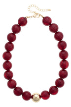 The Marjorie Fall Beaded Necklace by Canvas Style showcases large round red resin beads accented with a single central gold bead, finished with a gold chain and clasp for secure fastening.