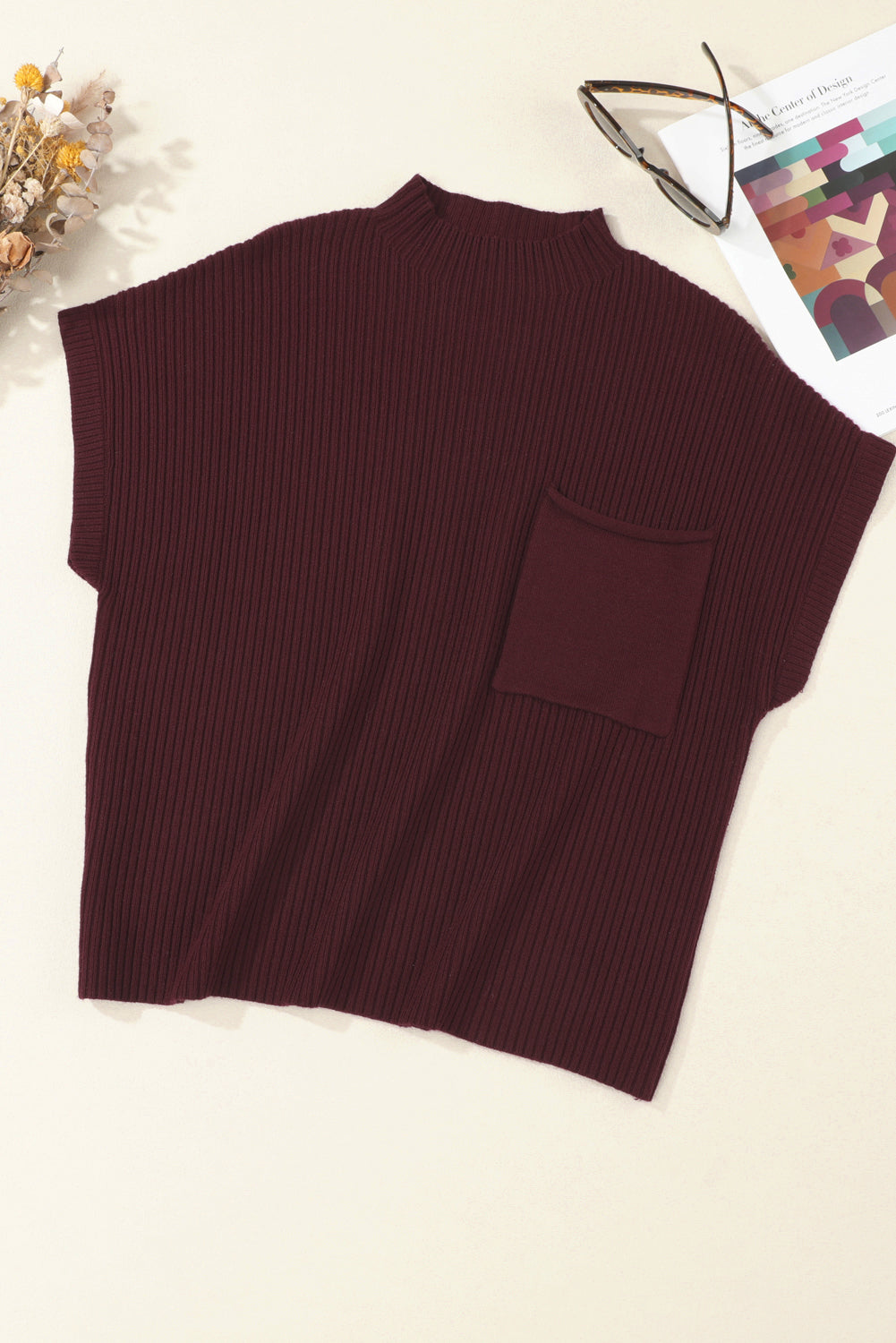 The Shewin Patch Pocket Ribbed Knit Short Sleeve Sweater in maroon is ideal for transitional weather. Styled with sunglasses, a magazine, and dried flowers, it creates a chic scene.