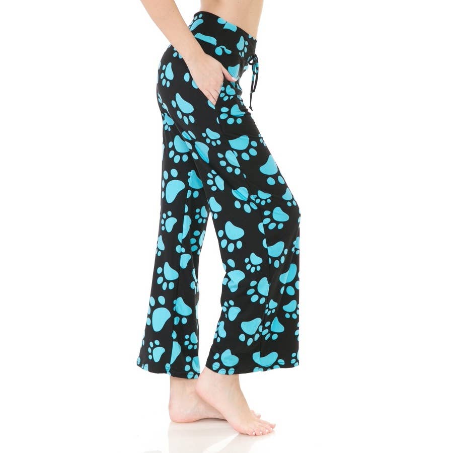 A person stands barefoot on a white background wearing Leggings Depot’s Buttery Soft Print Pajama Pants with blue paw prints and an elastic waistband.