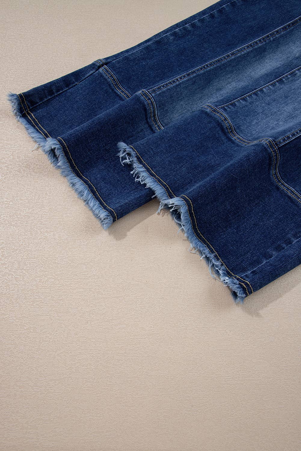 A close-up of the raw hem on 1 the Woman’s Drawstring Seam Detail Raw Hem Wide Leg Denim Pants in dark blue, displayed on a light textured surface.