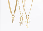 Three gold necklaces by WJW displayed on a white background: one featuring a clasp with crystal detailing, one adorned with a crystal bow charm, and the 18K Gold PVD Paperclip Carabiner Necklace showcasing a sleek gold bow charm.
