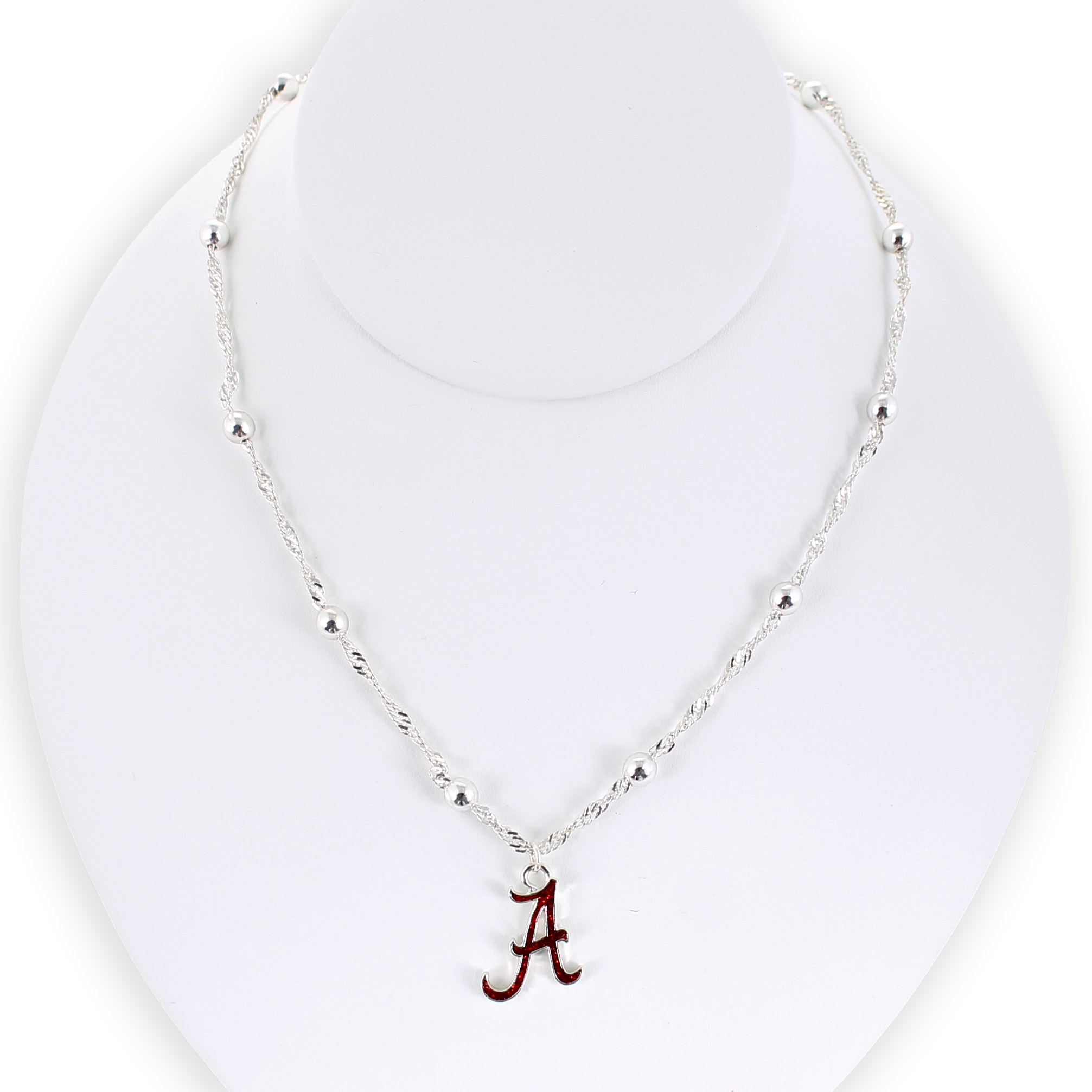 Show your school pride with the Alabama Glitter Enamel Logo Necklace by Seasons Jewelry. This silver beaded necklace features a crimson “A” logo pendant accented with sparkling glitter enamel, beautifully displayed on a white necklace stand—a shimmering tribute to University of Alabama spirit.