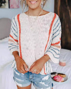 A woman is wearing the Rosa Clothing Boho Flared Sleeve Loose Knit Sweater, featuring white fabric with red and blue stripes, paired with distressed denim shorts, as she stands indoors with her hands clasped.
