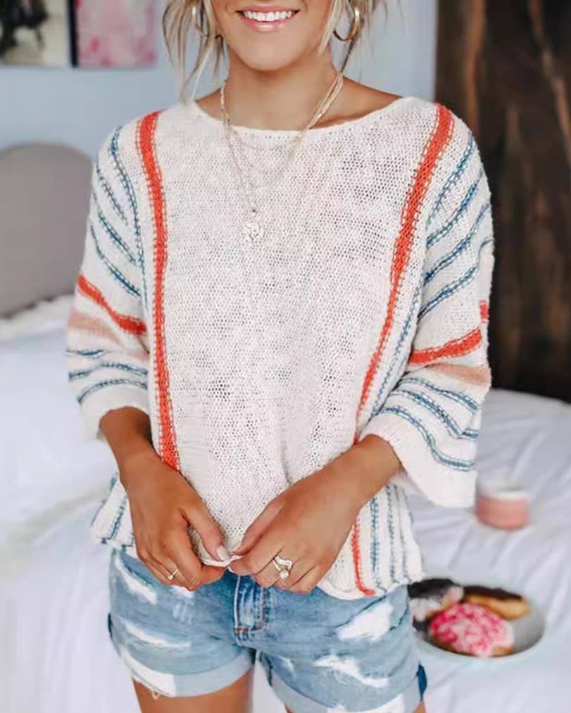 A woman is wearing the Rosa Clothing Boho Flared Sleeve Loose Knit Sweater, featuring white fabric with red and blue stripes, paired with distressed denim shorts, as she stands indoors with her hands clasped.