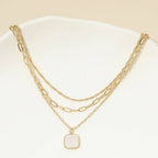 The Sensibling Corp. 18K Gold Dipped Square Pendant Accent Mixed Paperclip Chain Layered Necklace features three distinct gold-dipped chains, including a stylish square pendant and an adjustable extender, all elegantly arranged on a white surface.