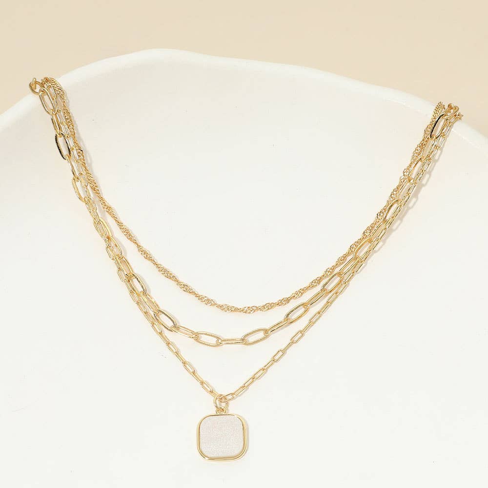 The Sensibling Corp. 18K Gold Dipped Square Pendant Accent Mixed Paperclip Chain Layered Necklace features three distinct gold-dipped chains, including a stylish square pendant and an adjustable extender, all elegantly arranged on a white surface.