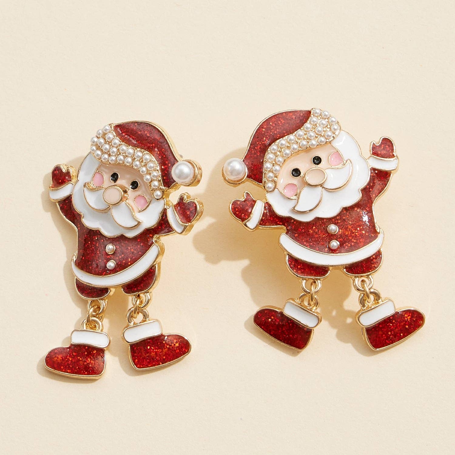 Add a festive touch to your outfit with the Enamel Glitter Santa Dangle Earrings from Lilla Haven—these statement holiday earrings showcase charming Santa Claus shapes with red glitter enamel, gold accents, pearl details, and playful dangling legs. Photographed on a cream background, they’re the perfect cheerful accessory for the season. Main image