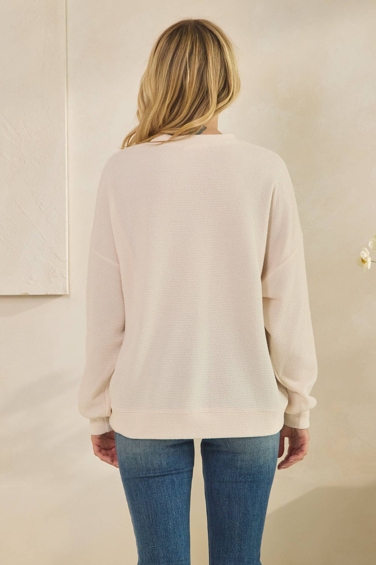 Back view of a person wearing a cream-colored ALABAMA Cloudy Soft Knit Long Sleeve Top and blue jeans.