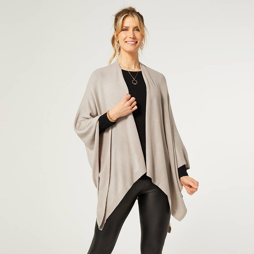 A woman smiles, wearing the COCO + CARMEN Kiara Light Weight Wrap over a black top and black leather-look pants against a plain white background.