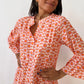 A person in a Shewin Orange Floral Button V Neck Bell Sleeve Mini Dress stands smiling with hands on hips, the boho floral print accentuating its V-neckline against a plain background.