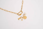Showcase your unique style with the WJW 18K Gold PVD Paperclip Carabiner Necklace, featuring three customizable charms—a pearl, a round gold pendant engraved with a lightning bolt, and two petite gold tags—all elegantly suspended from a sleek paperclip chain. Presented on a crisp white background.
