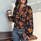 A Navy and Orange Print Pull Over Blouse in a navy, long-sleeved floral print, worn with blue jeans while holding a coffee cup and a clutch; a lightweight long sleeve top for fall.