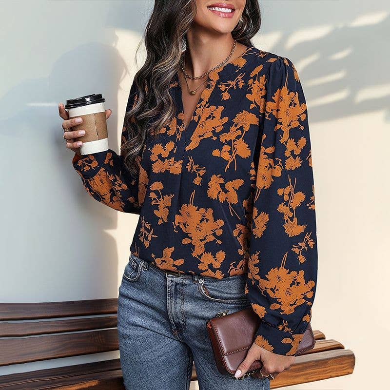 A Navy and Orange Print Pull Over Blouse in a navy, long-sleeved floral print, worn with blue jeans while holding a coffee cup and a clutch; a lightweight long sleeve top for fall.
