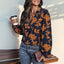 A Navy and Orange Print Pull Over Blouse in a navy, long-sleeved floral print, worn with blue jeans while holding a coffee cup and a clutch; a lightweight long sleeve top for fall.