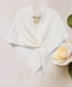 The JC Sunny Fashion Cashmere-Blend Knit Triangle Shawl features a cross-front design, elegantly tied at the center and styled on a light surface beside a white rose and green leaves for a chic look.