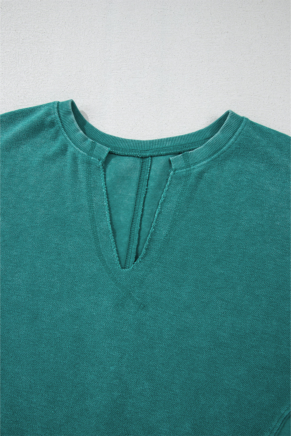 A Notched Neck Exposed Seam Drop Shoulder Sweatshirt from Shewin in a teal hue lies flat on a surface, showcasing its high-quality fabric.