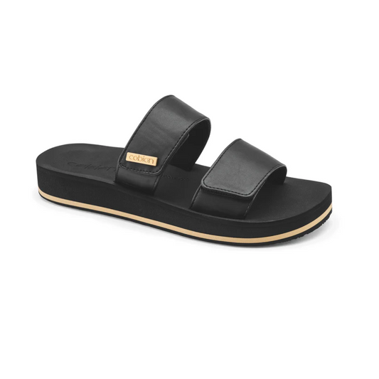 A Dana Rise Slide Sandal in Black by COBIAN with two thick, adjustable straps and a small gold-colored label on one strap, featuring a flat sole and an open-toe design. This elevated flatform slide combines comfort with style.