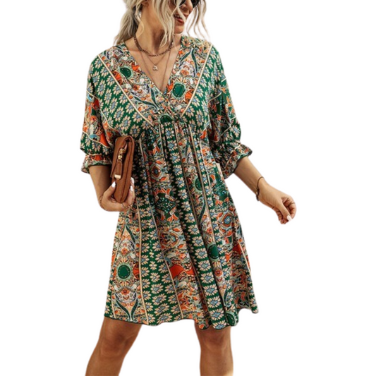 A woman wearing a V-Neck Half Sleeve Graphic Swing Dress in green, orange, and white from FASHION GO holds a brown clutch and looks to the side.