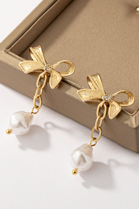 FASHION GO's Bowtie Stud with Pearl Drop Earrings in a beige jewelry box, highlighted by natural lighting.