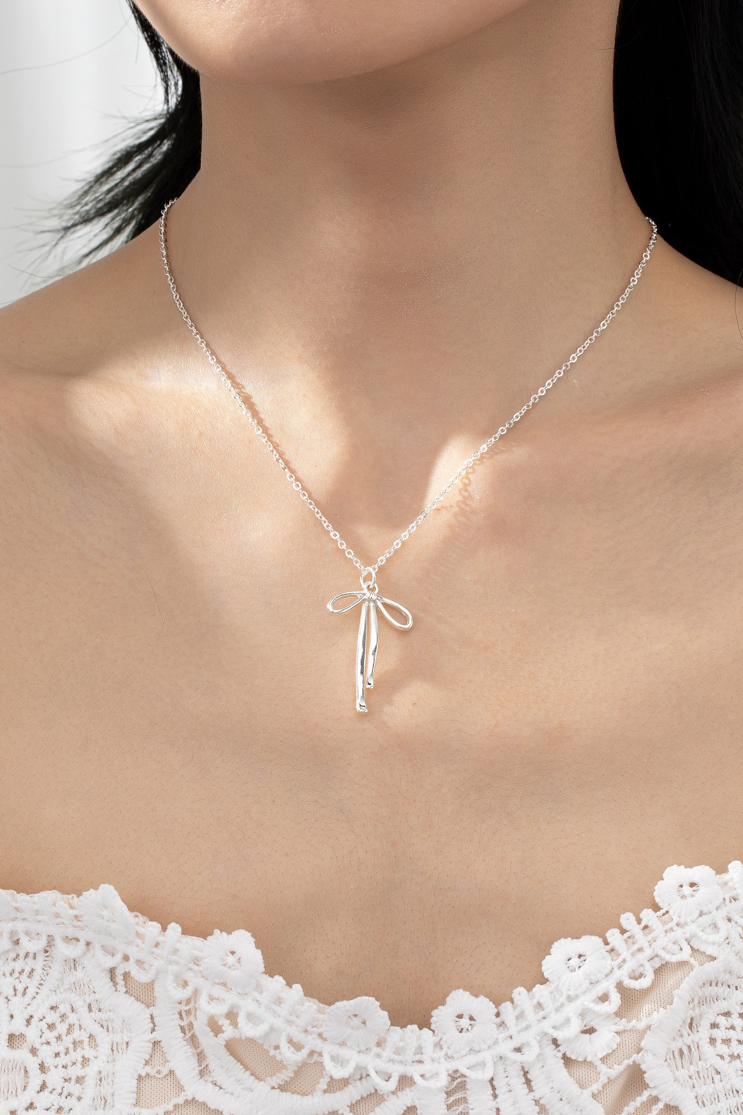 Close-up of a woman's neck wearing a delicate FASHION GO Brass Bow Pendant Necklace, against a lace top. Main image