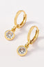 Pair of brass huggie hoops with a dangling round CZ pendant on a white background by FASHION GO.