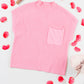 The Shewin Patch Pocket Ribbed Knit Short Sleeve Sweater, featuring a pink shade and a pocket, is displayed with red flower petals and a small gift box on a white background, ideal for transitional weather.