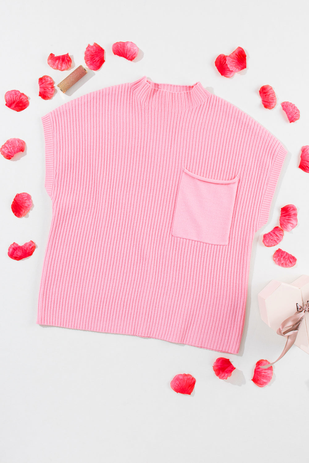 The Shewin Patch Pocket Ribbed Knit Short Sleeve Sweater, featuring a pink shade and a pocket, is displayed with red flower petals and a small gift box on a white background, ideal for transitional weather.