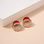 The Lilla Haven Pearl Santa Claus Stud Earrings, featuring charming red hats and beaded white beards, are displayed on a cream-colored surface beside a white rectangular object—making these Christmas Holiday Earrings the perfect seasonal accessory or thoughtful holiday gift.