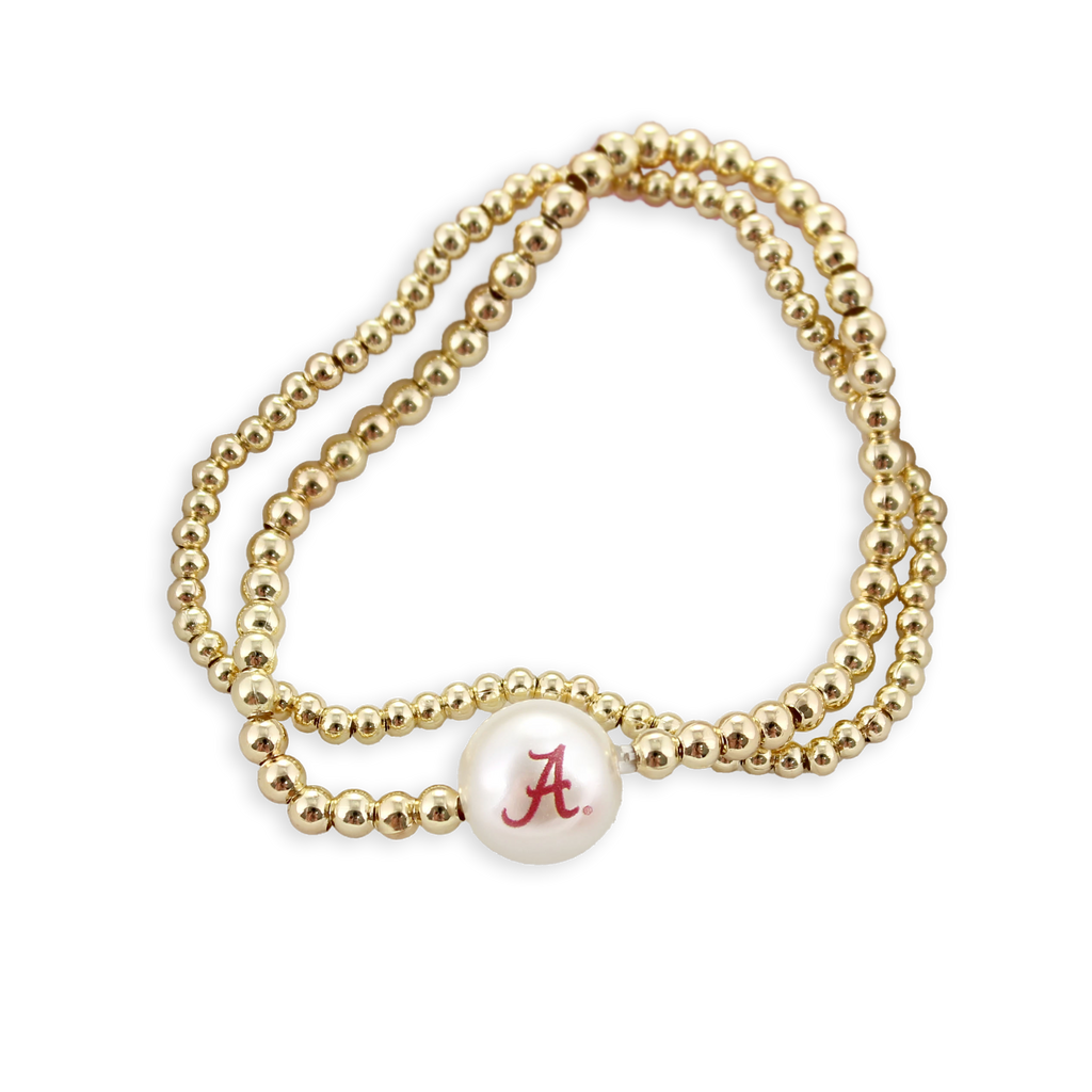 Seasons Jewelry’s Alabama Gold & Pearl Logo Stretch Bracelet Set is displayed on a white background—a subtle yet stylish accessory featuring gold beading and a single white bead with a red “A,” perfect for any University of Alabama fan.