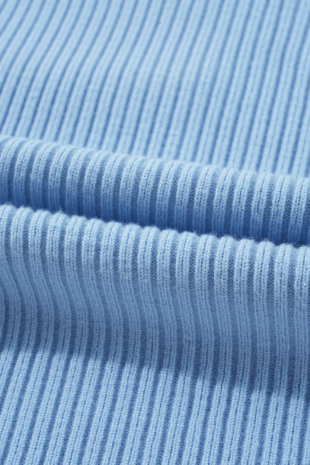 Close-up of a soft-textured light blue knit fabric, similar to Shewin's Patch Pocket Ribbed Knit Short Sleeve Sweater, with horizontal folds.