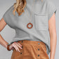 A person in a Shewin Patch Pocket Ribbed Knit Short Sleeve Sweater pairs it with a brown buttoned skirt. They have long hair and wear a pendant necklace and brown bracelet.