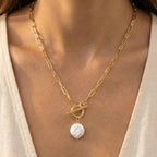 A person wears Anarchy Street's Toggle Chain Link Disc Pearl Charm Necklace, featuring a modern update on the classic pearl charm with a single white irregular-shaped pearl pendant.
