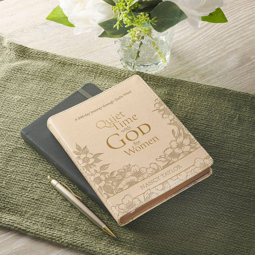 A beige, floral-embossed Devotional Quiet Time with God for Women Faux Leather book resting on a dark notebook with a pen nearby.