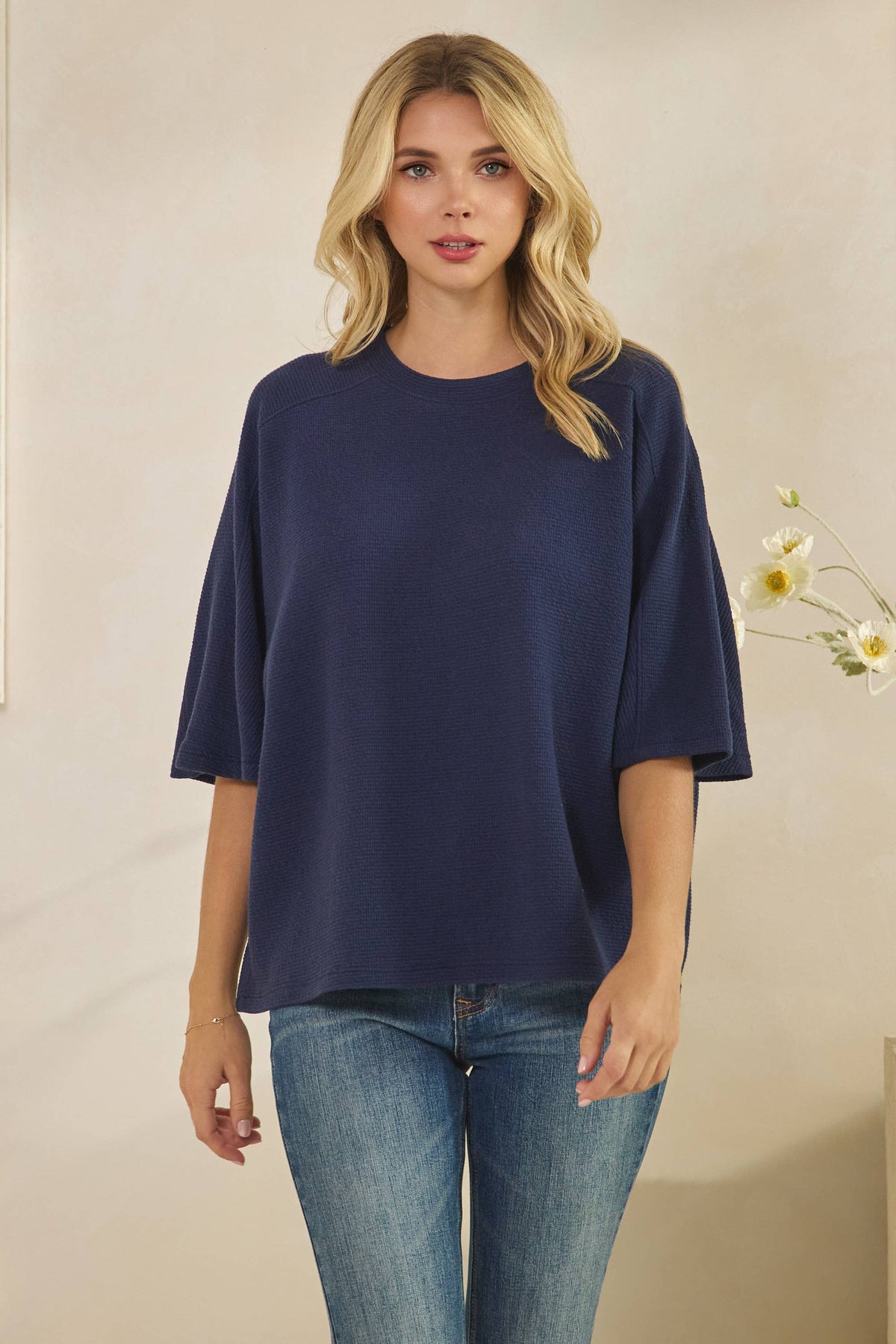 A person wears a navy blue CLOUDY KNIT 3/4 SLEEVE ROUND NECK TOP paired with blue jeans.