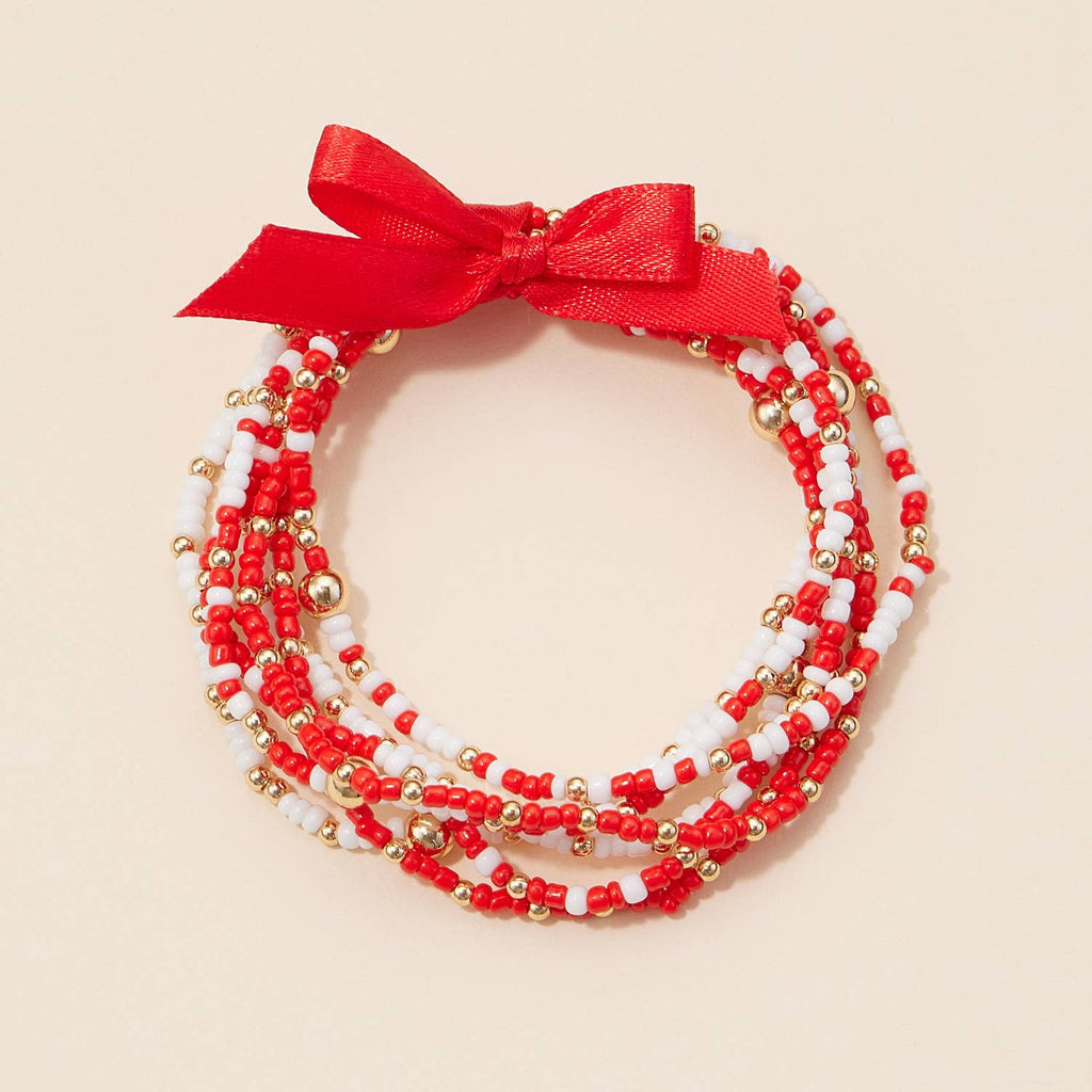 A Game Day Seed Beaded Bracelet Set stacked in red, white, and gold, tied together with a red ribbon bow.
