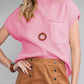 A woman wears a pink short-sleeve top and brown buttoned skirt, complemented by a pendant necklace and bracelet. For transitional weather, add the Shewin Patch Pocket Ribbed Knit Short Sleeve Sweater in cozy knit to enhance the look.