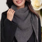 A woman in a dark coat smiles while holding her JC Sunny Fashion Cashmere-Blend Knit Triangle Shawl with Cross-Front Design. A white rose appears in the background.