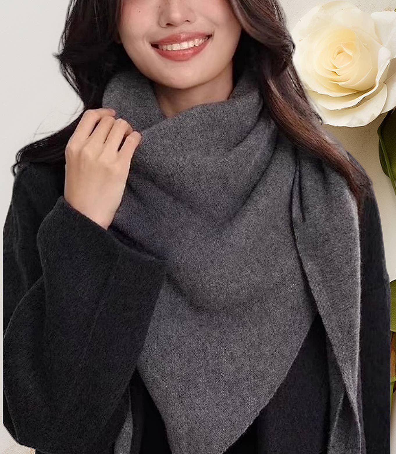 A woman in a dark coat smiles while holding her JC Sunny Fashion Cashmere-Blend Knit Triangle Shawl with Cross-Front Design. A white rose appears in the background.