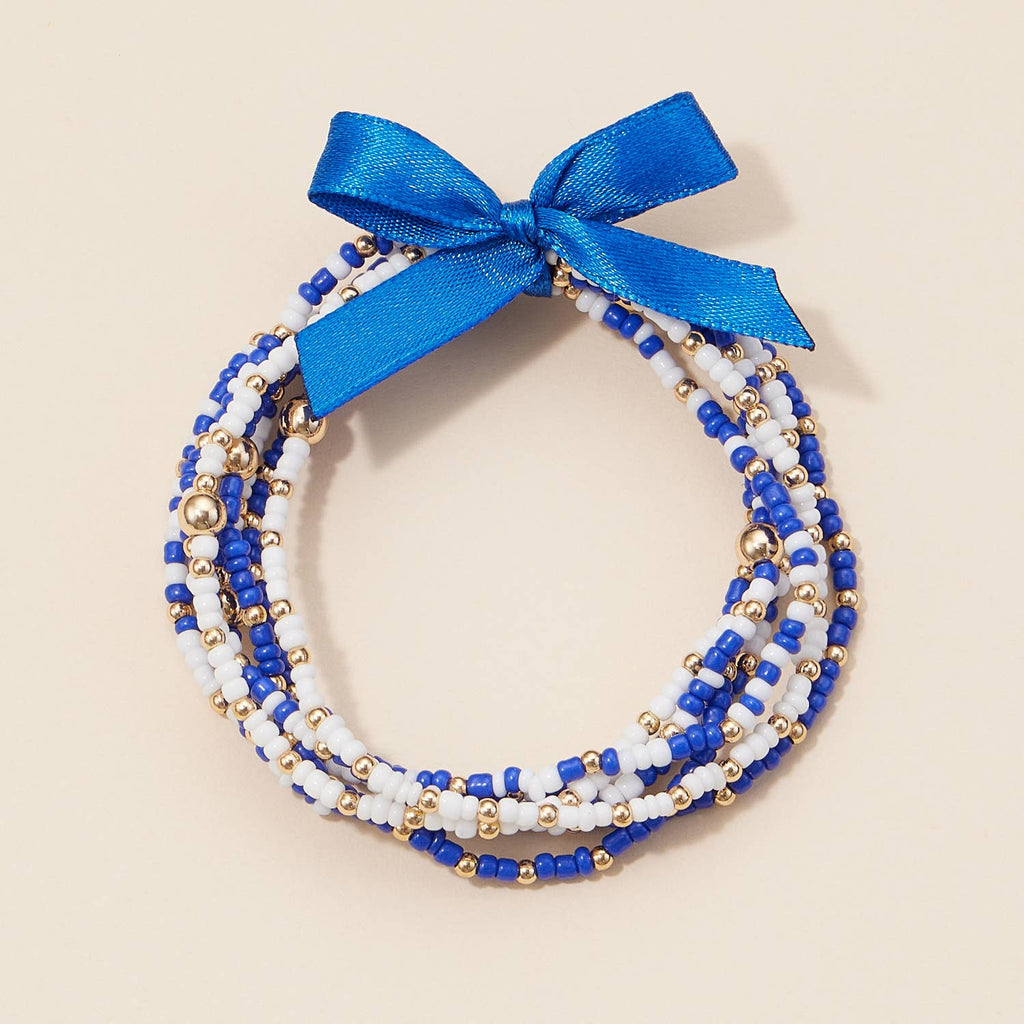 A stack of blue, white, and gold Game Day Seed Beaded Bracelet Set tied together with a blue ribbon bow.