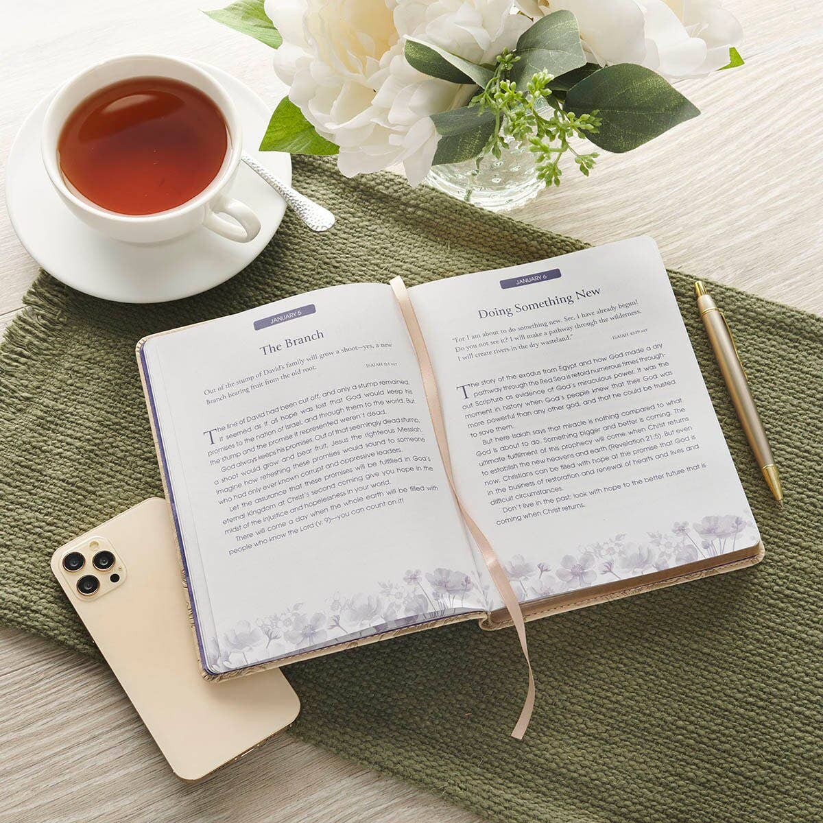 An open Devotional Quiet Time with God for Women Faux Leather book lying on a wooden table next to a cup of tea.