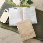 An open Devotional Quiet Time with God for Women Faux Leather book with gold embossed text on the cover, lying next to a smartphone on a textured surface.