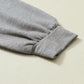 Close-up of the sleeve of the Khaki Color Block Exposed Seam Long Sleeve Top by Shewin, with a ribbed cuff and unique patchwork design, lying flat on a light-colored surface.