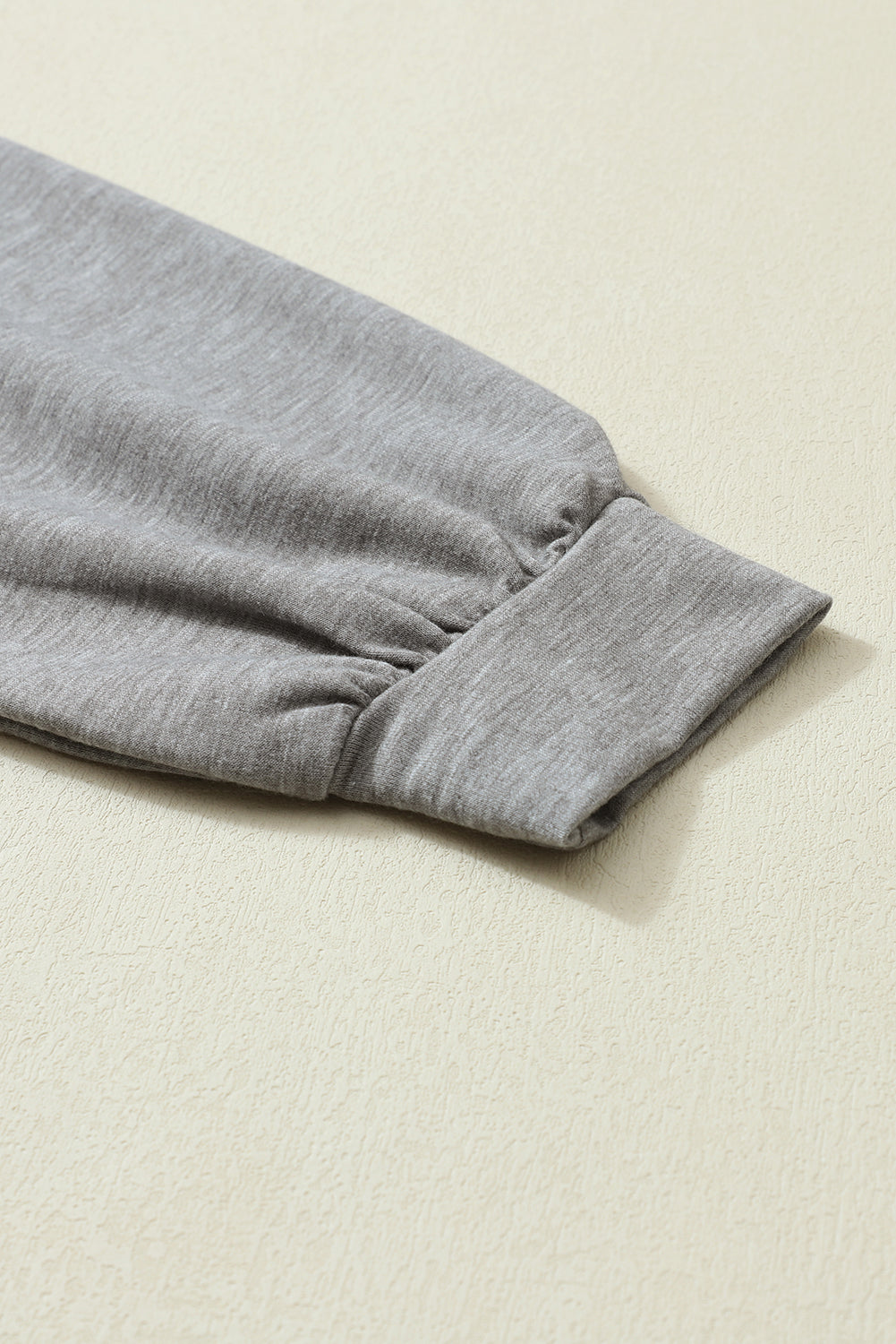 Close-up of the sleeve of the Khaki Color Block Exposed Seam Long Sleeve Top by Shewin, with a ribbed cuff and unique patchwork design, lying flat on a light-colored surface.