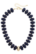 The San Sebastián Beaded Resin Necklace by Canvas Style is a statement piece featuring large dark blue resin beads, a single central gold bead, and is finished with a gold clasp and an adjustable chain.
