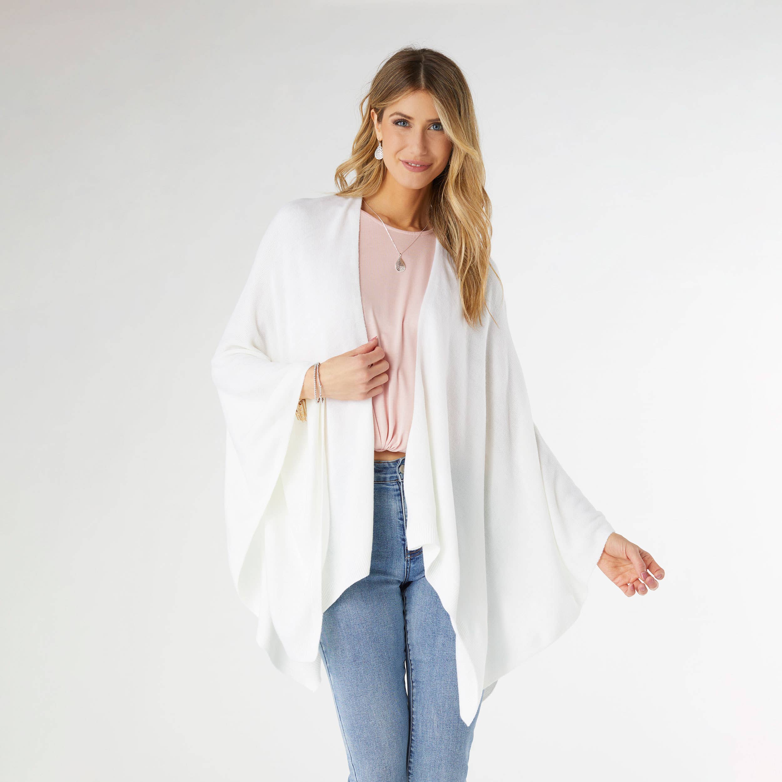 A woman stands against a plain background wearing the COCO + CARMEN Kiara Lightweight Wrap in white over a light pink top and blue jeans. This stylish, one-size-fits-most piece is perfect for effortless layering. Main image