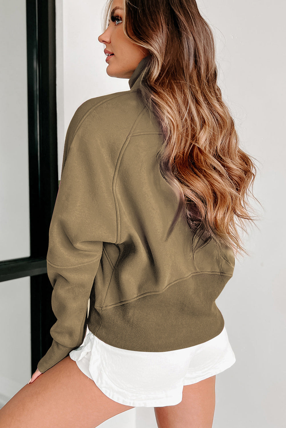 A woman with long wavy hair wears a Shewin gray zip-up stand collar ribbed thumbhole sleeve sweatshirt made of high-quality material and white shorts.