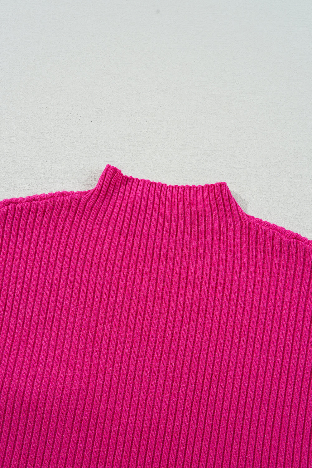 Close-up of a bright pink short sleeve sweater, crafted from cozy ribbed knit fabric by Shewin, against a light gray background.