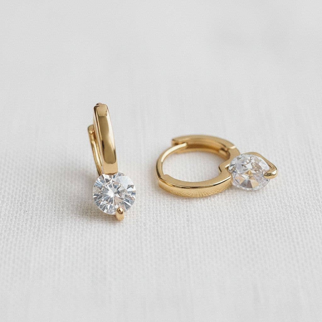 A pair of Ellemadera Modern Geometric Zirconia Drop Earrings, each adorned with a single round clear zirconia and featuring a subtle geometric design, displayed on a white textured surface.