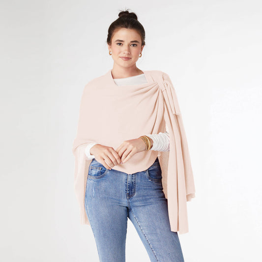 Woman wearing a light pink COCO + CARMEN Pull Thru Wrap over a white top and blue jeans, standing with hands together against a plain background—highlighting this chic accessory as a must-have for any wardrobe.
